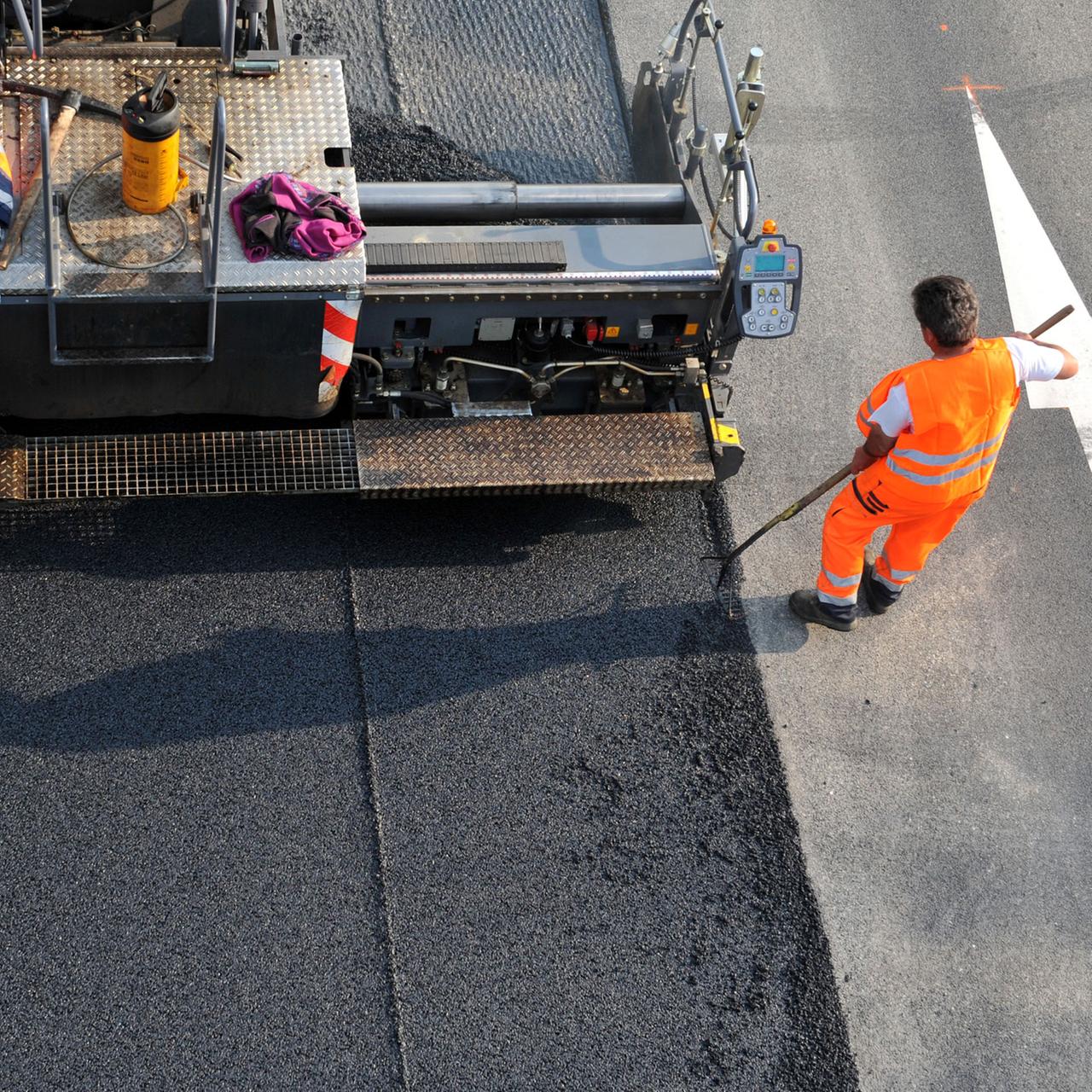 Ein Straßenbauer in orange-farbener Arbeitskleidung bringt eine neue Asphaltdecke auf einer Straße in Freiburg auf.