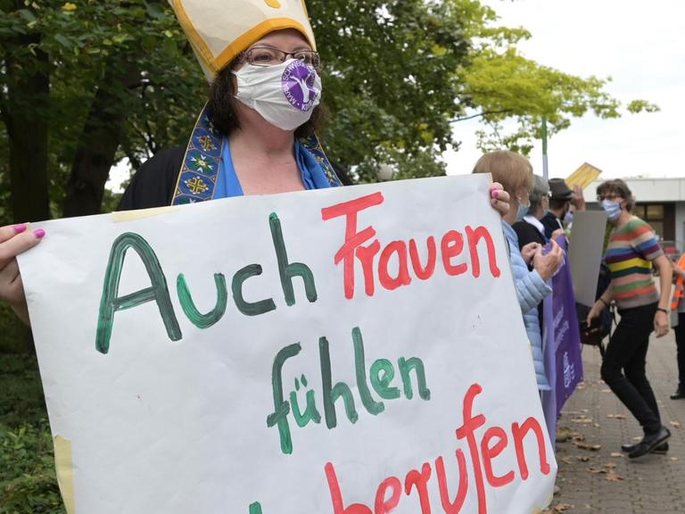 Demonstrantin vor der Regionalkonferenz des Synodalen Weges in Ludwigshafen. Sie trägt ein Transparent mit der Aufschrift "Auch Frauen fühlen sich berufen". © Synodaler Weg / Klaus Landry