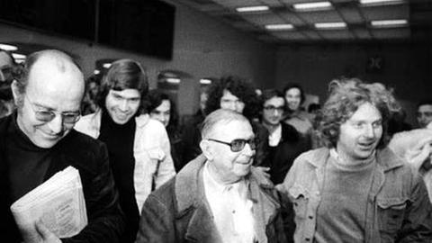 Schwarz-weiß-Aufnahme von Klaus Croissant, Jean-Paul Sartre und Daniel Cohn-Bendit in einem Gebäude, umringt von Menschen