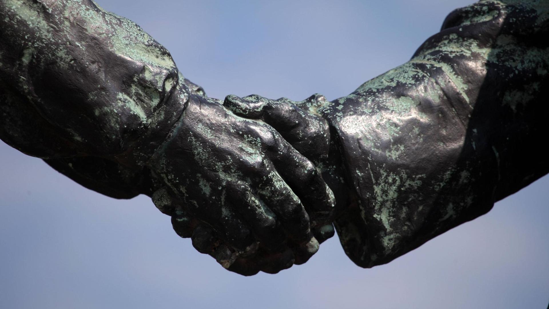 Zwei Hände von Bronzefiguren reichen einander die Hände.
