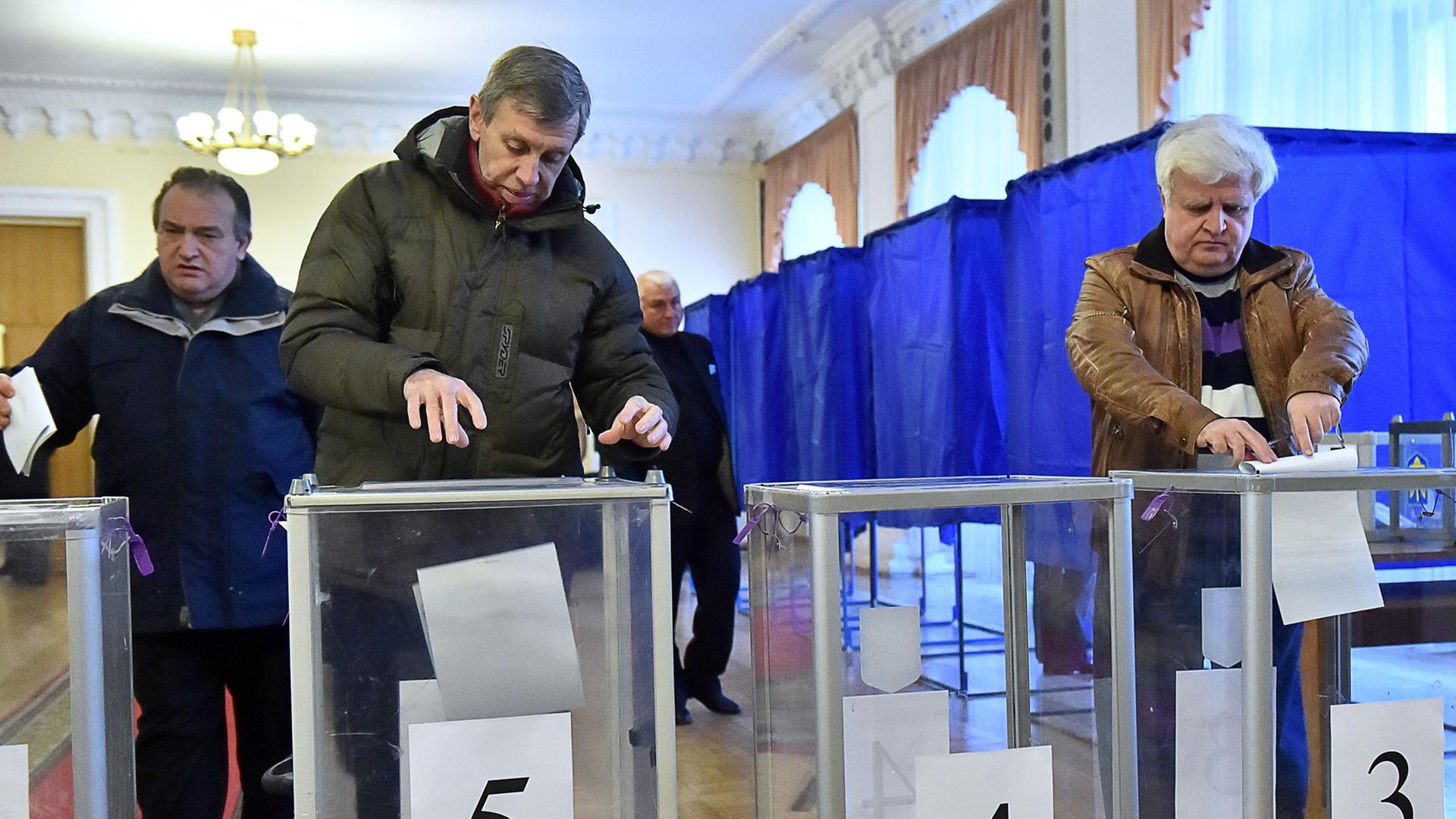 In einem Wahllokal in der ukrainischen Hauptstadt Kiew werfen zwei Männer und eine Frau ihre ausgefüllten Stimmzettel in die Wahlurnen.
