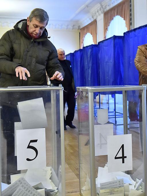 In einem Wahllokal in der ukrainischen Hauptstadt Kiew werfen zwei Männer und eine Frau ihre ausgefüllten Stimmzettel in die Wahlurnen.