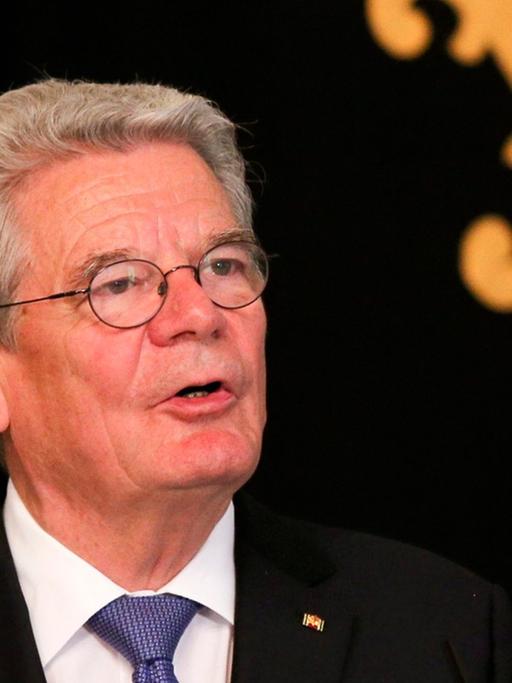 Joachim Gauck hält vor einem Wappen vor schwarzem Hintergrund eine Rede