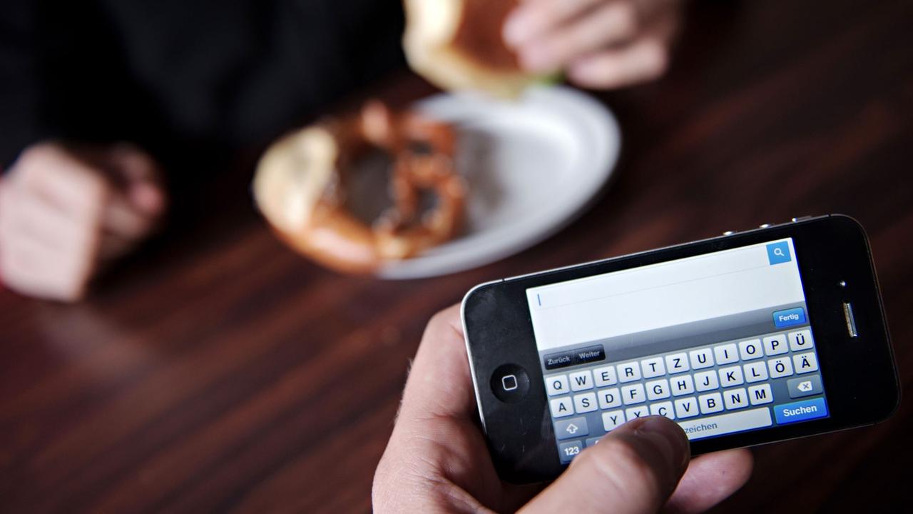 Ein Mann surft mit seinem Smartphone am Essenstisch im Internet. 