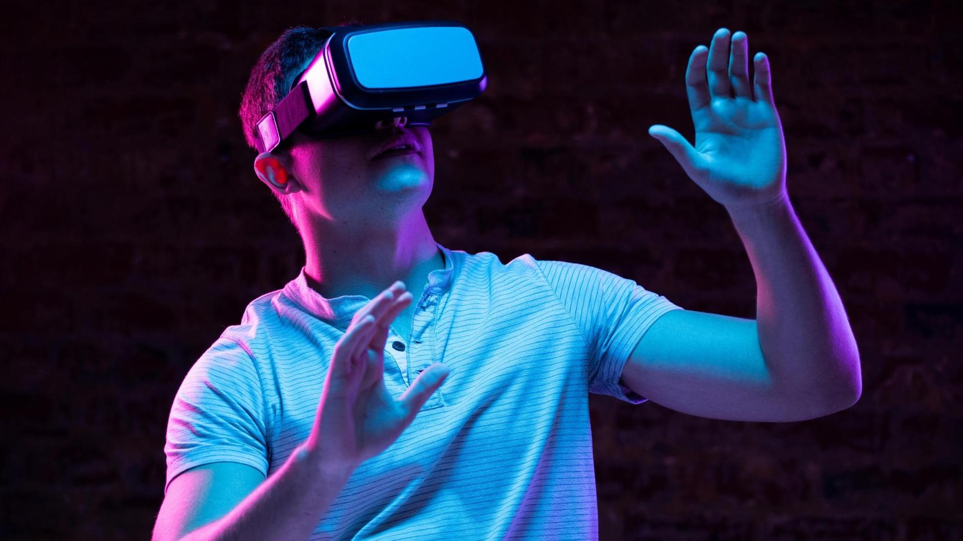 Ein Mann steht ein einem dunklen Raum trägt eine VR-Brille.