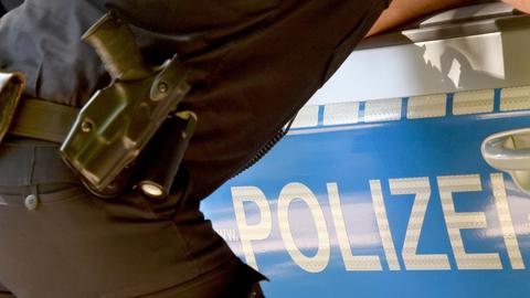 Ein Polizist mit Pistole im Halfter lehnt an einem Absperrgitter mit dem Schriftzug "Polizei".