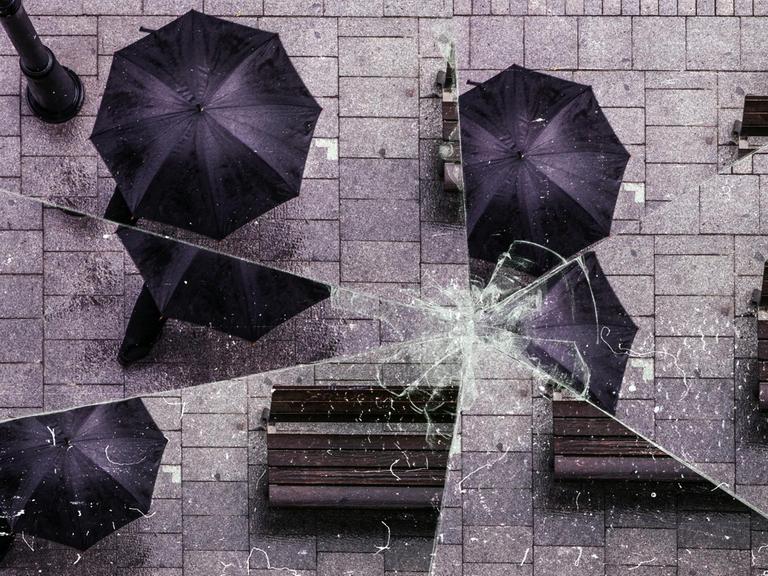 Bild einer Straße mit einem Mann unter einem schwarzen Regenschirm, aus der Vogelperspektive. Der Effekt eines zerbrochenen Spiegels ist über das Bild gelegt.