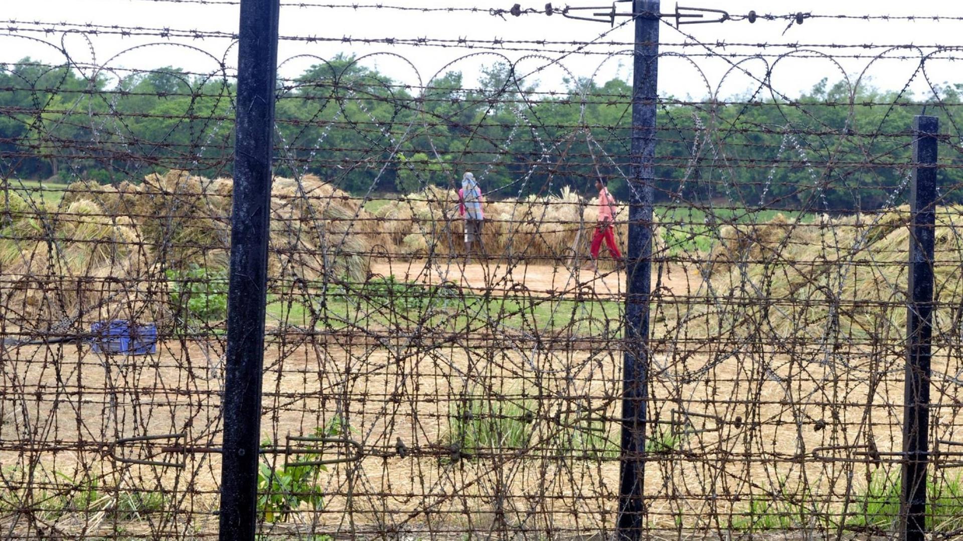 Indische Bauern arbeiten auf einem Feld direkt an der durch einen Zaun gesicherten Grenze.