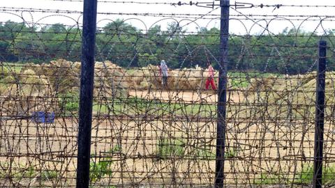 Bauern arbeiten auf einem Feld direkt an der durch einen Zaun gesicherten indisch-pakistanischen Grenze.