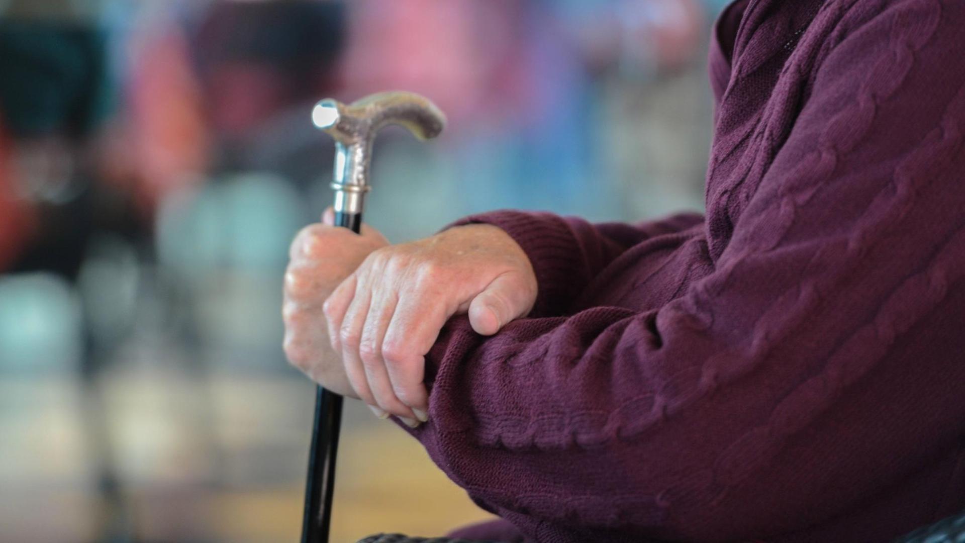 Ein alter Mann hält einen Gehstock mit Silbergriff.