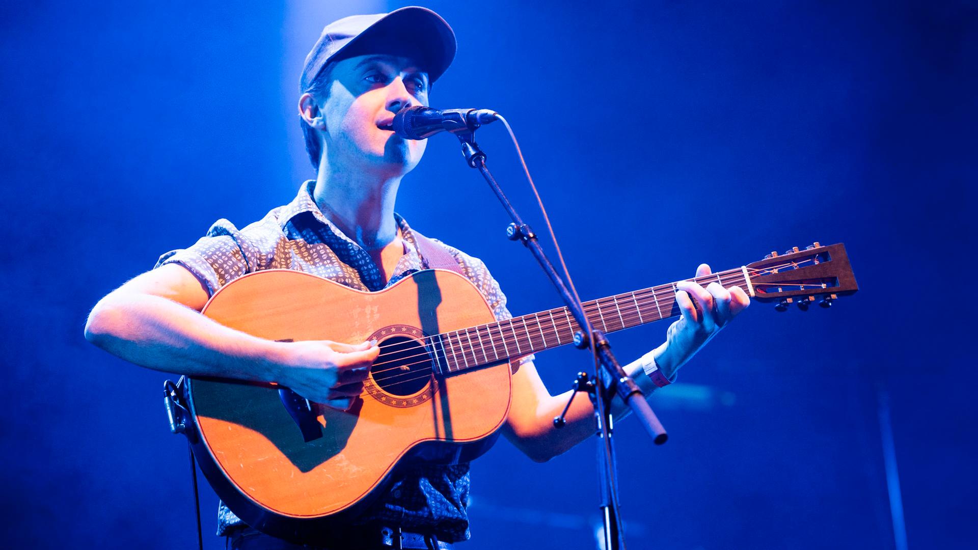 Ein Mann mit Gitarre steht auf einer Bühne und singt.