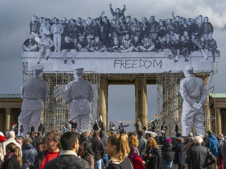 Der französische Street-Art-Künstler JR hat zum Tag der Deutschen Einheit 2018 eine Installation an das Brandenburger Tor heften lassen eine 25 Meter hohe, dreidimensionale Fotocollage. Die Aufnahmen stammen vom 10. November 1989, vom Tag nach dem Mauerfall.