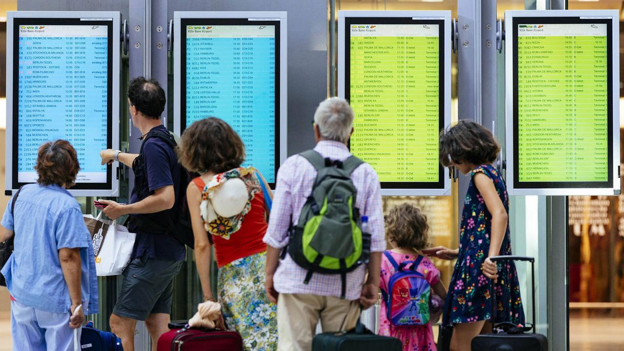 Flugpassagiere studieren Infotafeln für Ankunft und Abflug am Flughafen Köln/Bonn (16.7.2018).
