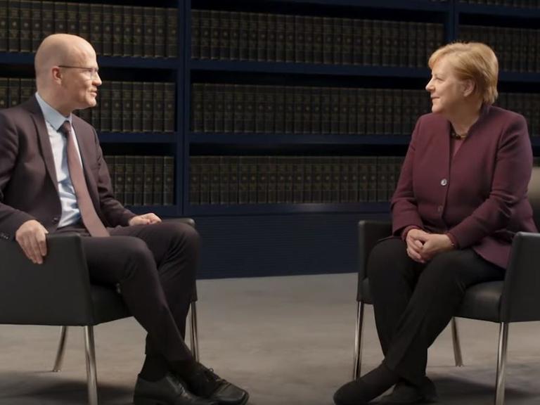 Angela Merkel und Ralph Brinkhaus sitzen einander auf einem Podium gegenüber.