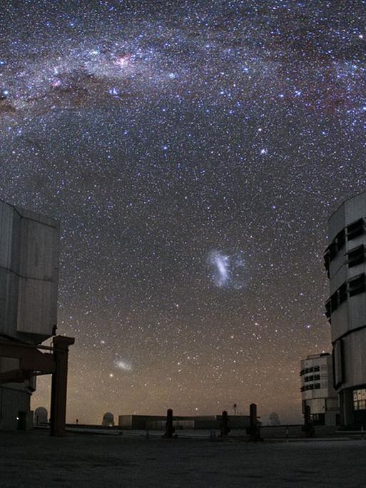 Die beiden Magellanschen Wolken am Südhimmel zwischen den Schutzbauten des Very Large Telescopes der ESO auf dem Cerro Paranal.
