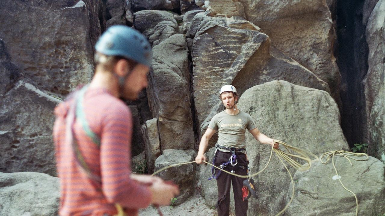 Zwei junge Männer mit Helm und mit Kletterausrüstung am Felsen stehend.