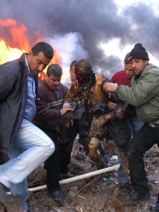 Libanesen retten einen mit Dreck beschmierten Überlebenden des Anschlags in Beirut, im Hintergrund lodern flammen.