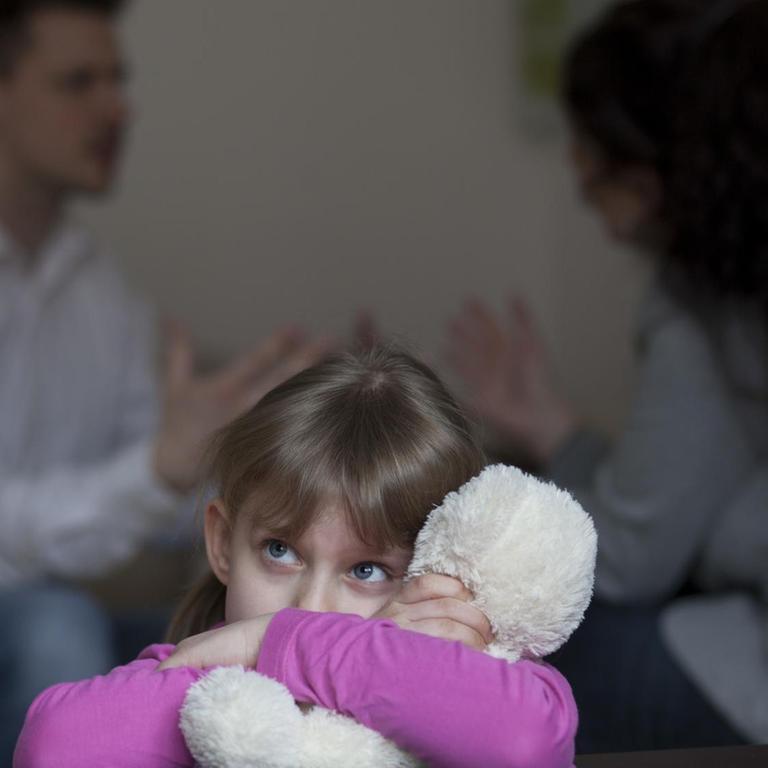 Zwei Erwachsene streiten sich in einer Wohnung, während die Tochter traurig ist (Symbolfoto). 