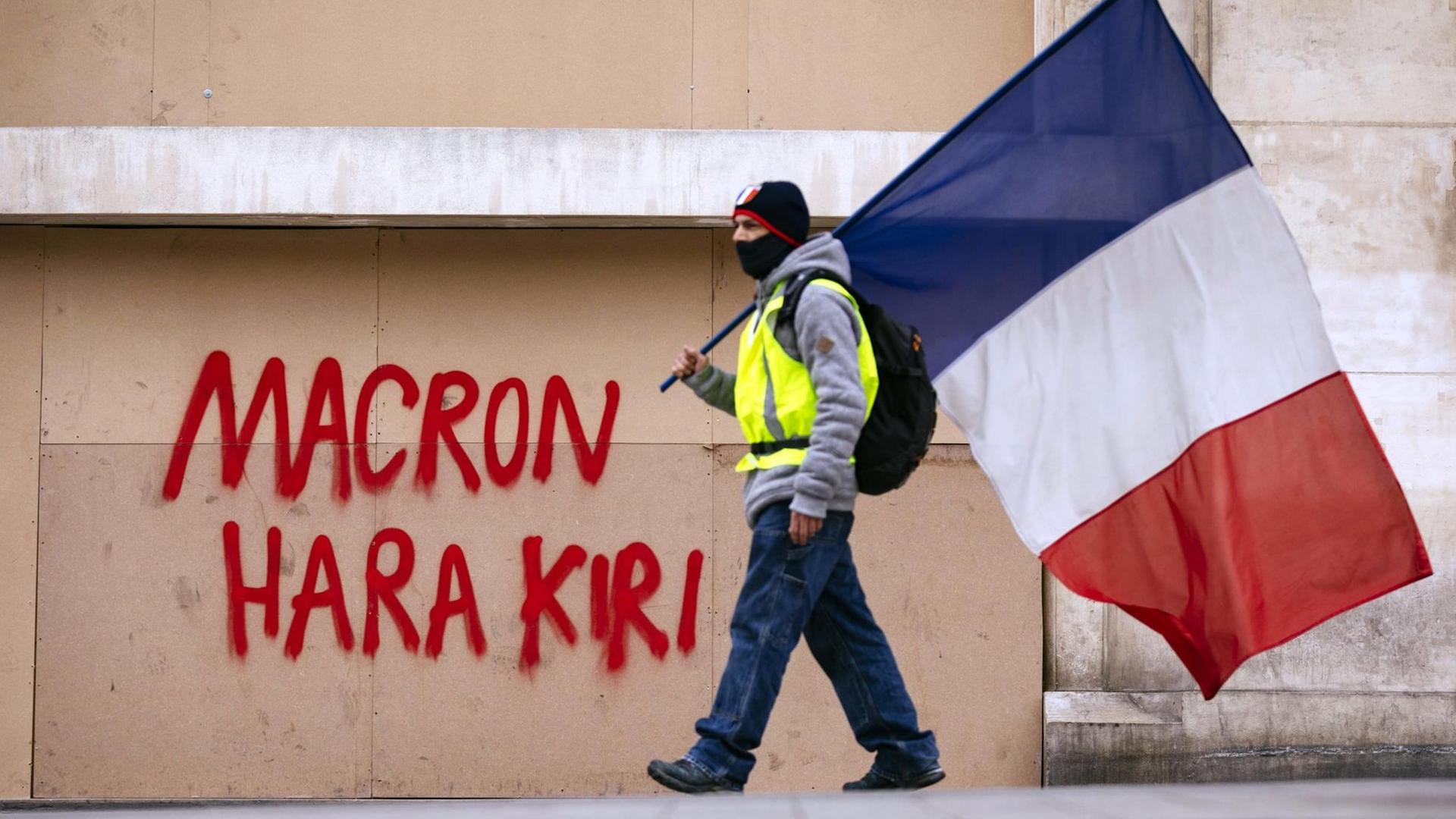 Ein Demonstrant der Gelb-Westen-Bewegung mit der französischen Fahne vor einer Mauer. Impression von den Gelbwesten-Protesten gegen Präsident Macron auf den Champs Elysées.