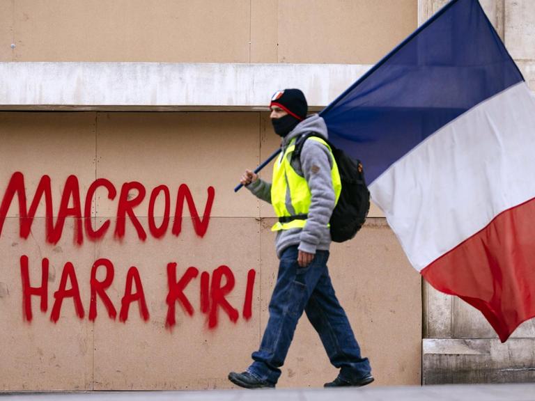 Ein Demonstrant der Gelb-Westen-Bewegung mit der französischen Fahne vor einer Mauer. Impression von den Gelbwesten-Protesten gegen Präsident Macron auf den Champs Elysées.