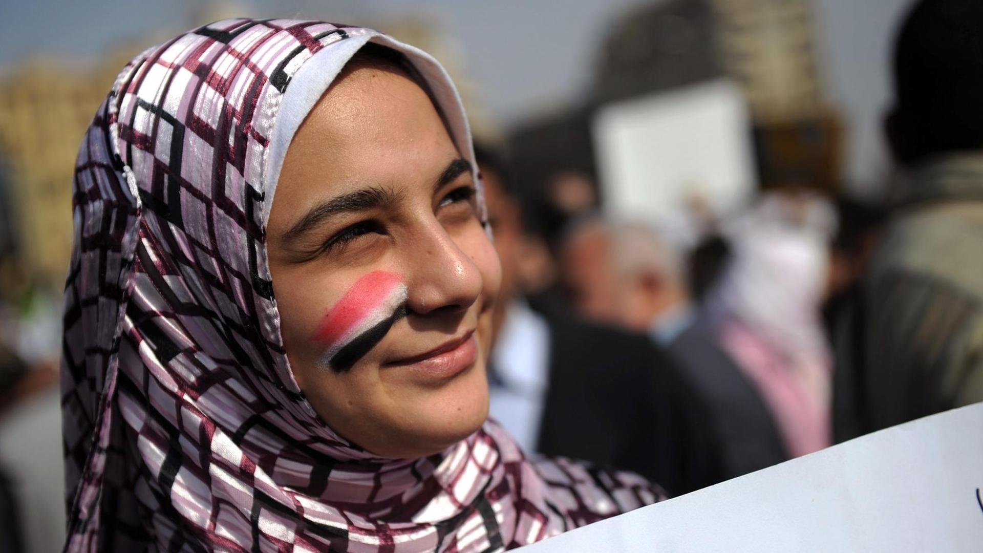 Eine junge Frau, die sich die ägyptischen Nationalfarben auf die Wange gemalt hat, steht mit einem Plakat inmitten der Demonstranten.