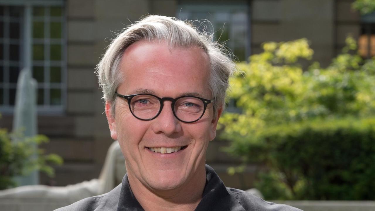 Marc-Oliver Hendriks, der geschäftsführende Intendant des Dreispartenhauses Staatstheater Stuttgart, blickt freundlich lächelnd in Richtung Betrachter.