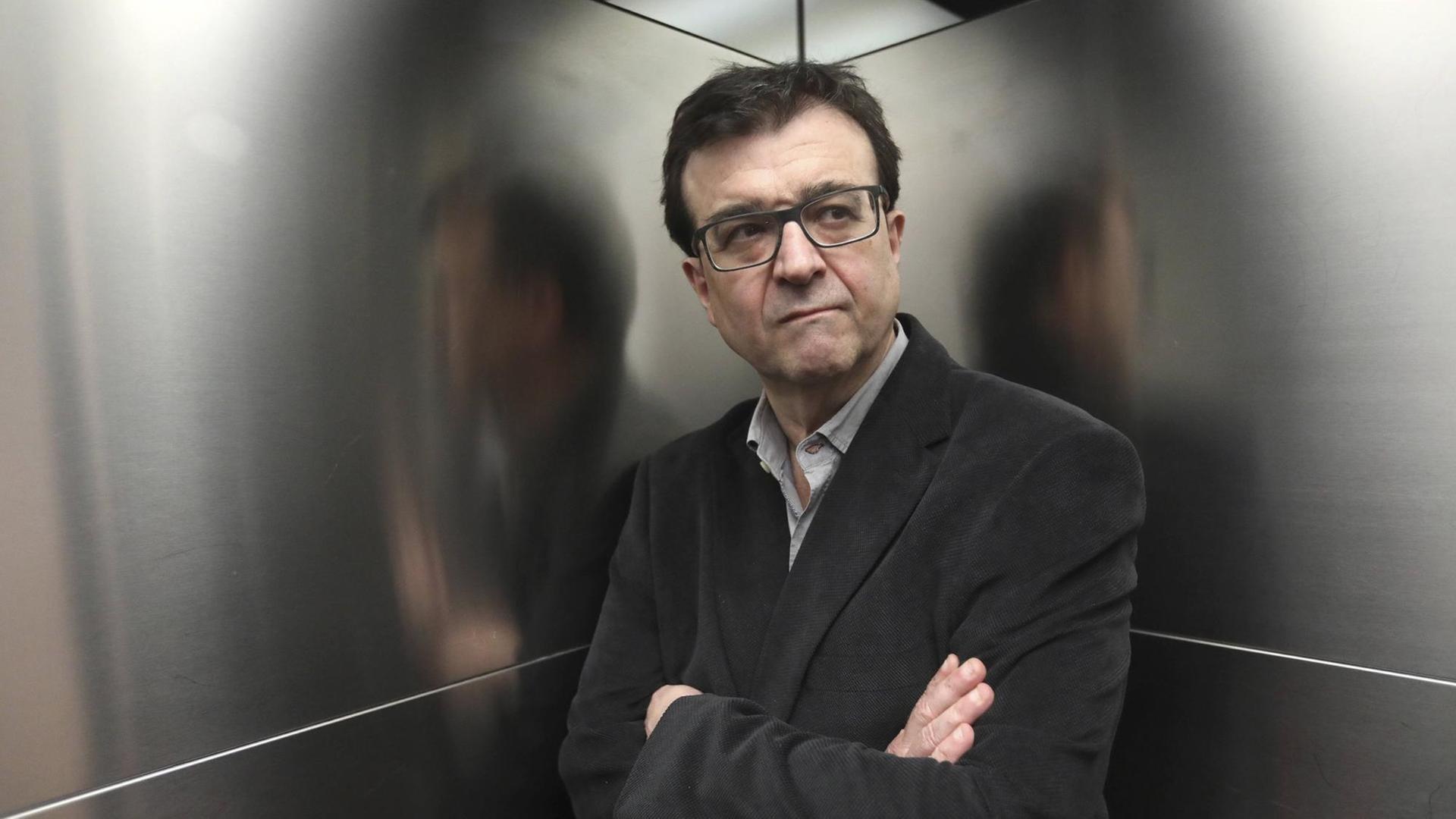 Der katalanische Schriftsteller Javier Cercas steht in der Ecke eines Aufzugs, er spiegelt sich in den silberglänzenden Wänden.