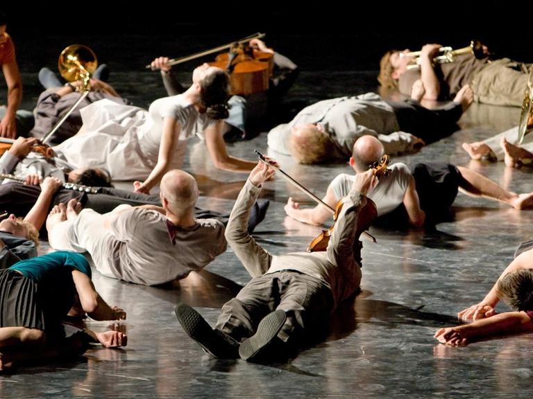 Musikerinnen und Musiker liegen mit ihren Instrumenten in den Händen auf einer Bühne.