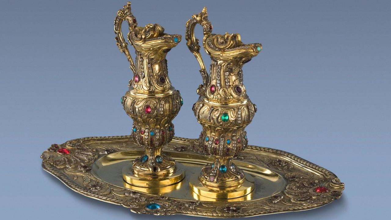 Zwei goldene Kännchen stehen auf einem goldenen Tablett. Alles ist reich mit Ornamenten und bunten Steinen verziert.