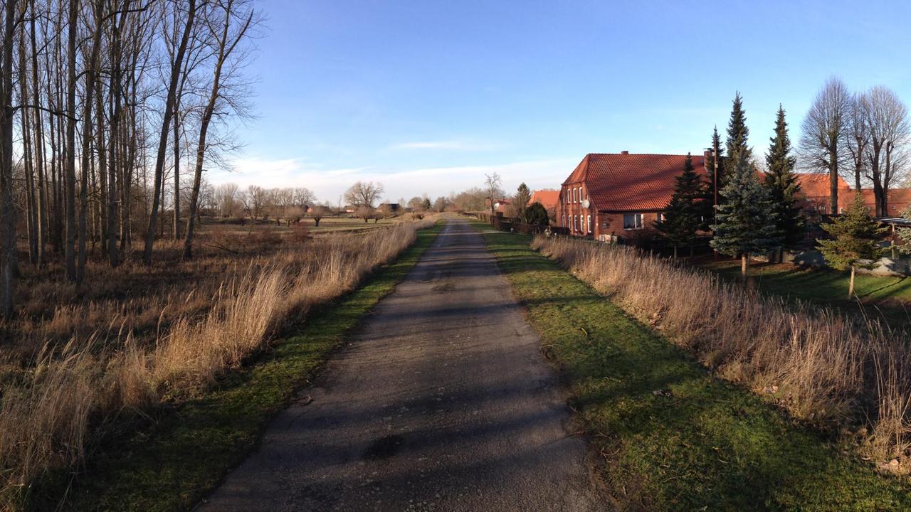 Ein Weg führt in die Ferne rechts von ihm liegt ein backsteinerner Hof, den die Abendsonne anleuchtet