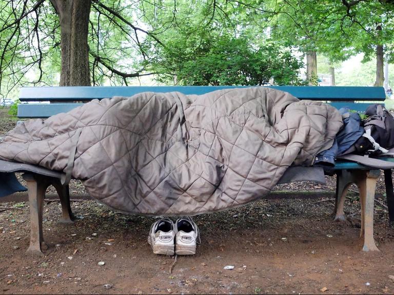 Ein Obdachloser schläft auf einer Bank in einem Park in Düsseldorf.
