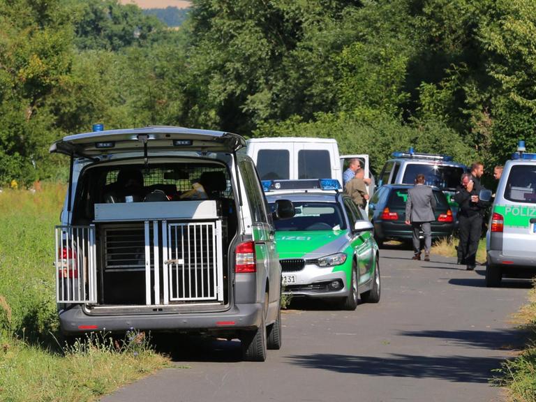 Polizisten stehen auf einem Weg bei Würzburg (Bayern) neben ihren Fahrzeugen.