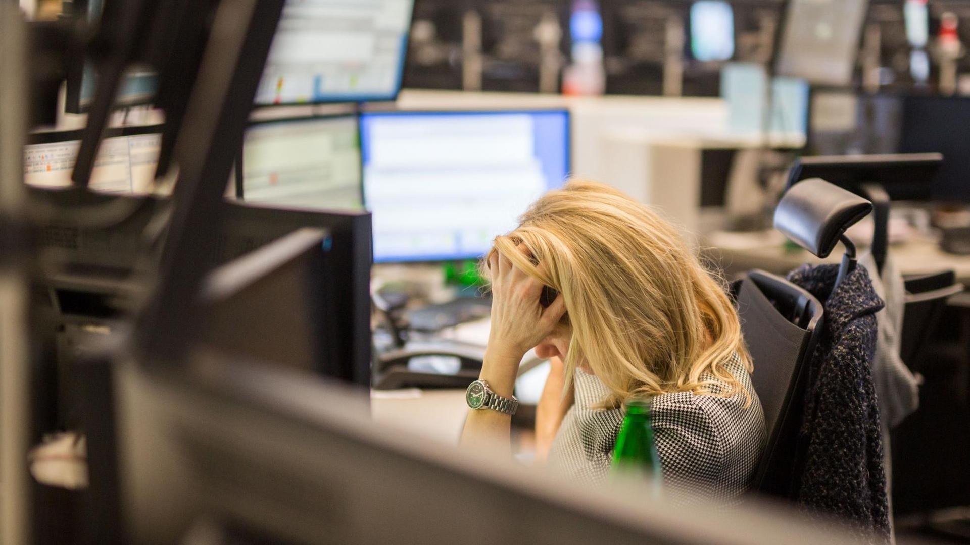 Eine Frau sitzt an ihrem Schreibtisch in der Frankfurter Börse und stützt den Kopf mit der Hand ab.
