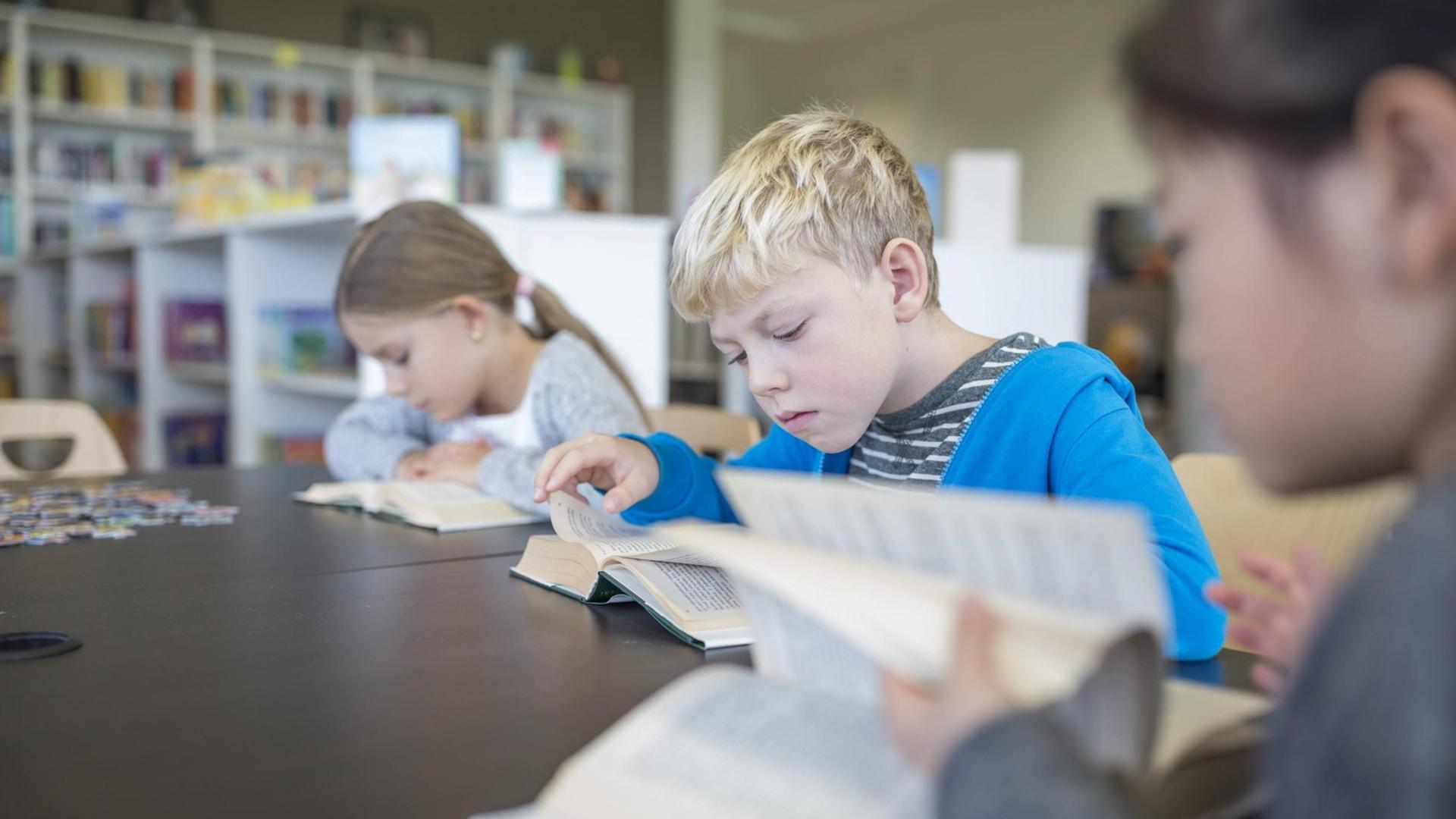Drei Schüler sitzen in der Schulbibliothek und lesen. Sie sind tief in ihre Bücher versunken. Auf dem Tisch liegt außerdem ein Puzzle.