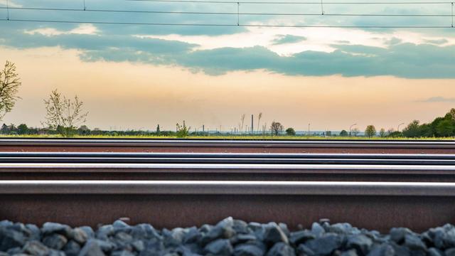 Gezeigt sind Eisenbahnschienen. Im Hintergrund eine grüne Wiese und leicht bewölkter Himmel.