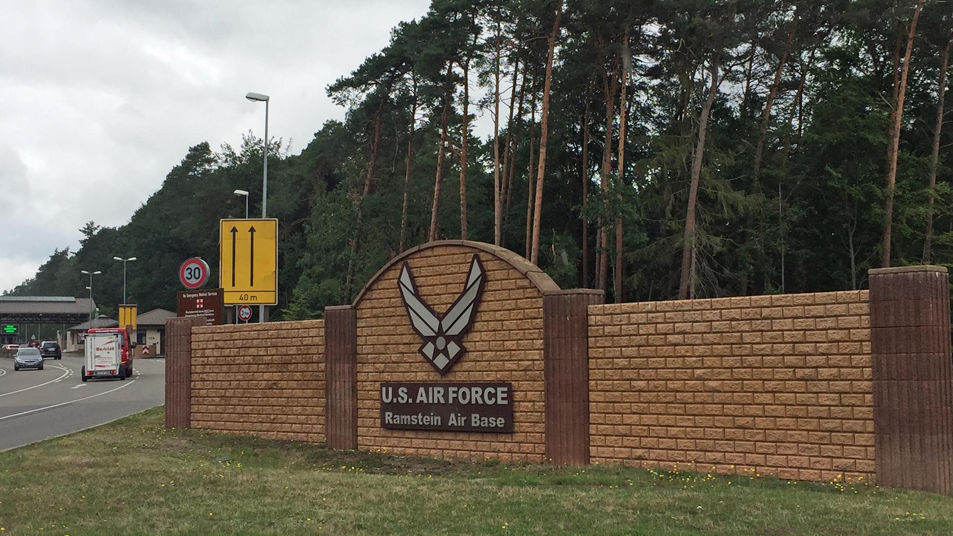 Auf einer Mauer am Straßenrand steht der Name der Air Base Ramstein. Darüber ist ein militärisches Logo angebracht.