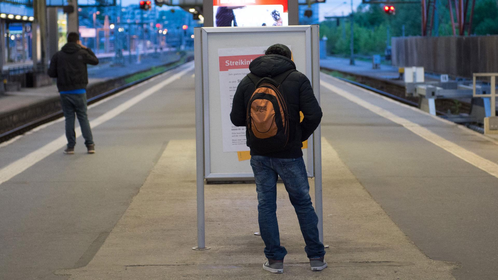 Ein Mann steht am im Bahnhof in Stuttgart an einem Bahnsteig vor einem Poster mit der Aufschrift "Streikinformation". Der Bahnsteig ist fast leer. Außer dem Mann steht ein anderer Mann auf einem Gleis.
