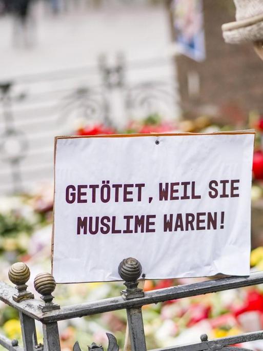 Eine Frau steht auf dem Marktplatz in Hanau vor dem Denkmal der Brüder Grimm. Vor dem Denkmal stehen Blumen, Kerzen und ein Plakat mit der Aufschrift «Getötet, weil sie Muslime waren».