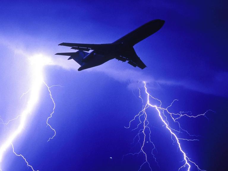 Ein Flugzeug fliegt durch eine Gewitterwolke. Im Hintergrund blitzt es.