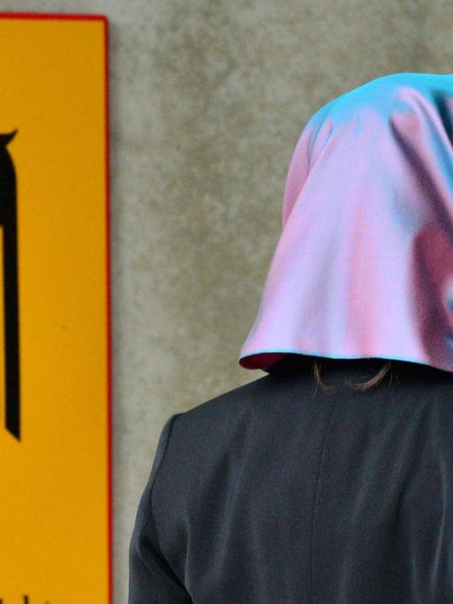 Eine junge Frau mit Kopftuch, die Klägerin, läuft am 24.09.2014 in Erfurt (Thüringen) am Behördenschild mit der Aufschrift "Bundesarbeitsgericht" vorbei.