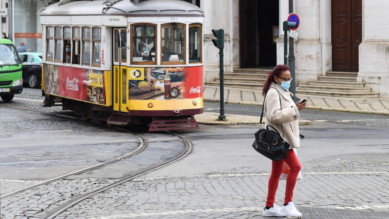 Frau mit Mund-Nasen-Bedeckung vor Straßenbahn in Lissabon.