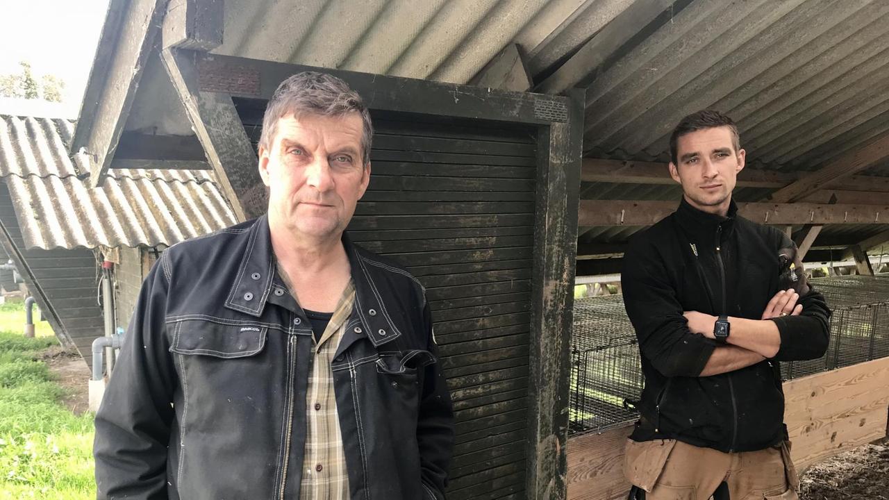 Ein älterer und ein junger Mann stehen am Eingang eines Stalls. Der junge verschränkt vor den Käfigen stehend die Arme.