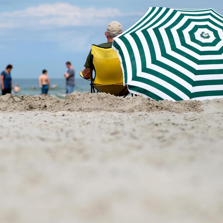 Urlauber sitzen bei hochsommerlichen Temperaturen unter einem Sonnenschirm am Strand von Norderney.