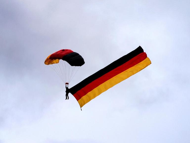 Ein Fallschirmspringer zieht am 02.10.2016 eine Deutschlandfahne am Himmel über dem Bürgerfest in Dresden (Sachsen) hinter sich her.