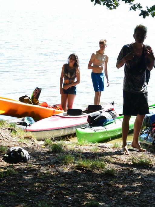 Eine Gruppe Jugendlicher steht an einem See in Brandenburg. Hier haben sie auch ihre Kajaks liegen. Sie nehmen an einem Projekt teil, bei dem es darum geht, mit wenig Geld Herausforderungen zu bewältigen. Foto: Deutschlandfunk/Dieter Wulf