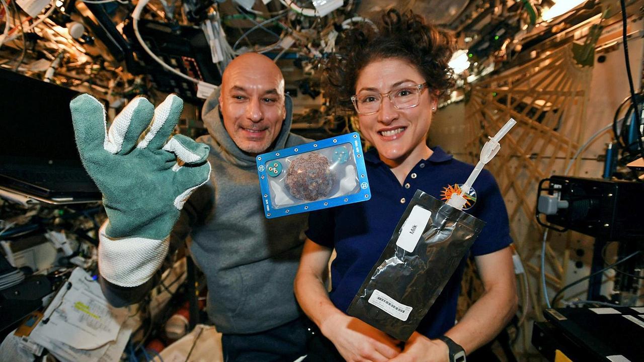 Backen auf der ISS: Christina Koch (r), Astronautin aus den USA, und Luca Parmitano, Astronaut aus Italien, mit einem Keks, der in der  ISS gebacken wurde. 