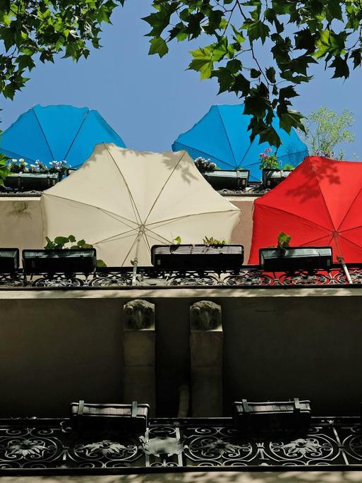 Regenschirme stehen auf Balkonen eines Wohnhauses an einem sonnigen Tag in Berlin.