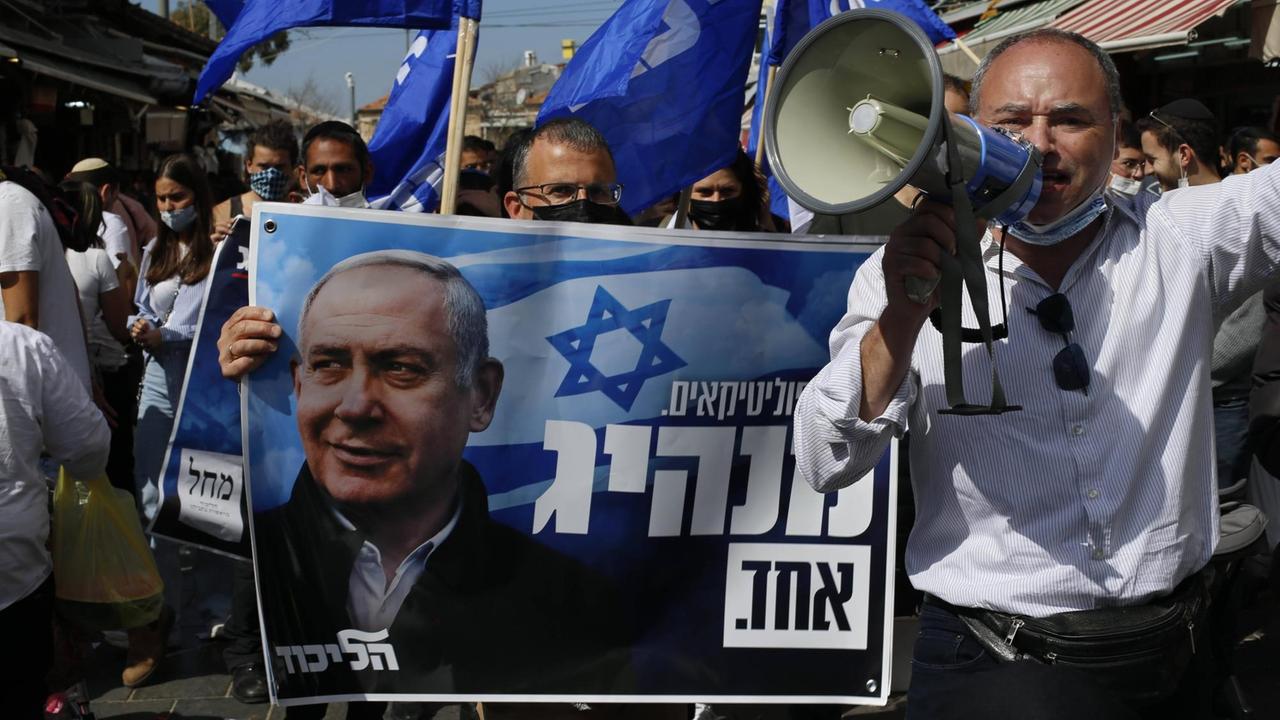 Anhänger der Likud Partei im Wahlkampf auf der Strasse in Jerusalem auf palästinensischem Gebiet. Sie halten einen Banner mit Premierminister Benjamin Netanyahu in den Händen. 19. März 2021.