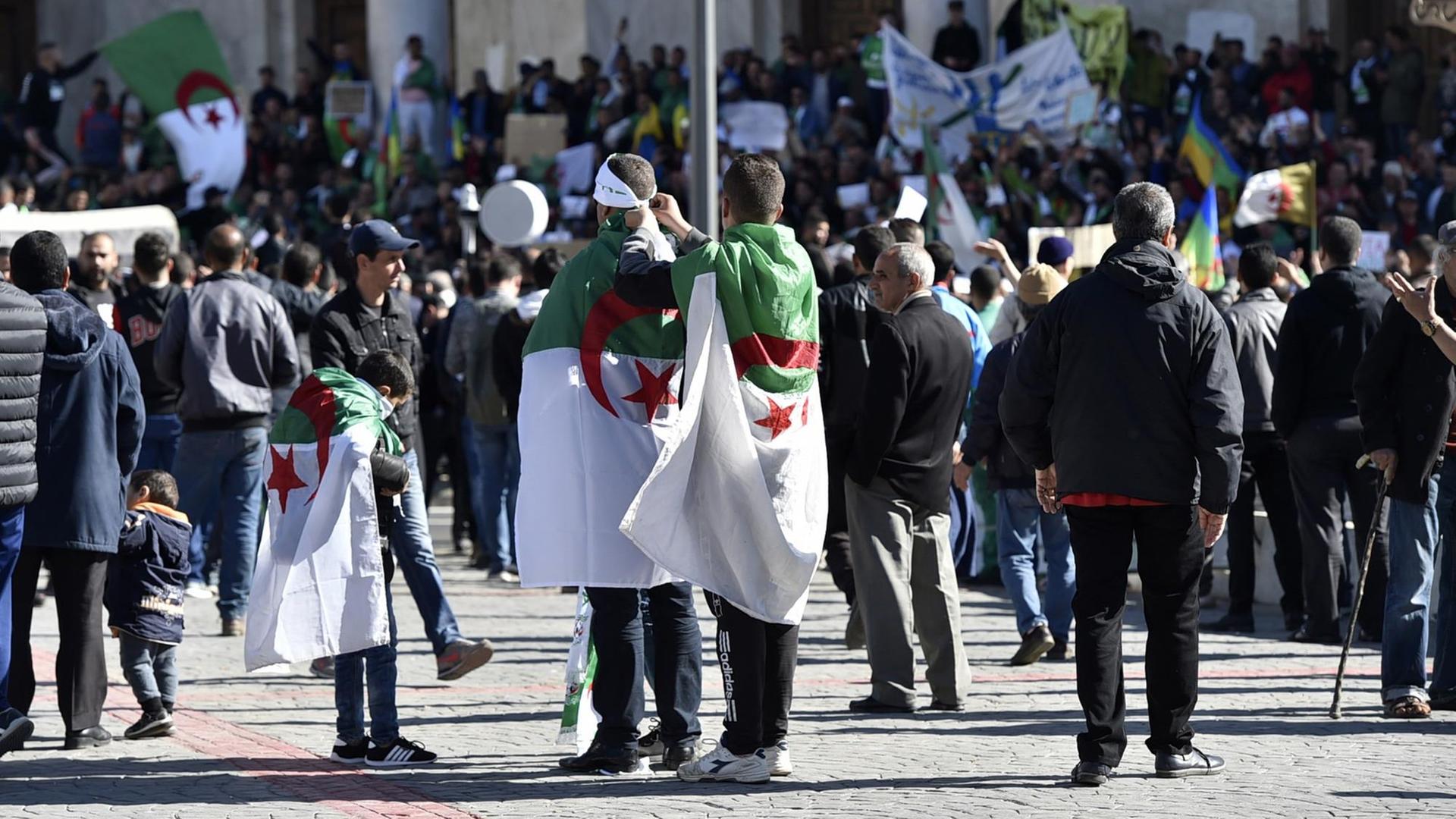 In Algier versammeln sich Menschen zu Protesten gegen Präsident Bouteflika, einige sind in algerische Flaggen gehüllt.