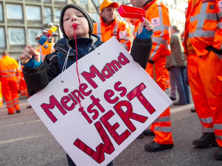 Ein Junge hält während eines Warnstreiks ein Plakat mit der Aufschrift "Meine Mama ist es Wert"